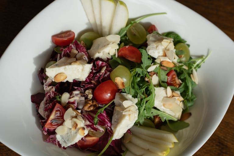 Colorful salad with brie cheese, grapes, and almonds on a white plate.